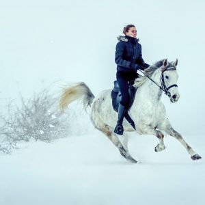 Girl rides horse in falling snow at dusk