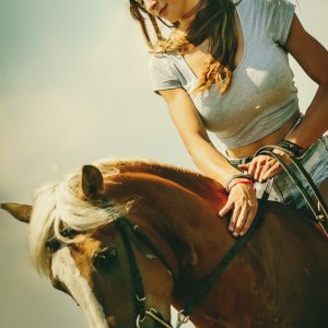 A beautiful girl is sitting on a horse and stroking it